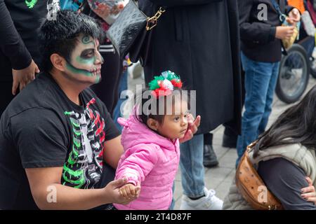 Detroit, Michigan – Ein Mann und ein Kind beobachten Tänzer bei der Day of the Dead-Feier im Valade Park am Detroit Riverfront. Stockfoto