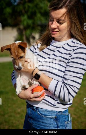 Die Frau hält ihren Hund an den Händen und umschließt ihn. Glückliche Besitzerin umarmt und küsst süße Freundin. Tierpflege Stockfoto