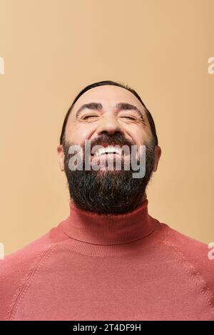 Lächelnder Mann mit Bart in rosa Rollkragenpullover, der fröhlich vor beigefarbenem Hintergrund lächelt Stockfoto