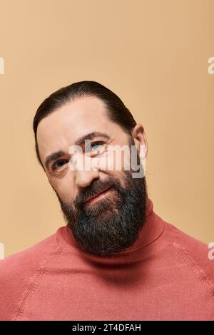 Lächelnder Mann mit Bart in rosa Rollkragenpullover, der fröhlich vor beigefarbenem Hintergrund lächelt Stockfoto