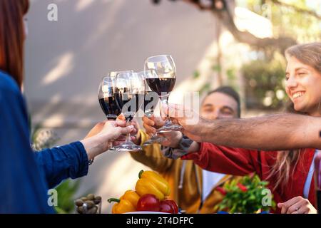 Eine Gruppe von Freunden hebt ihre Weingläser in einem fröhlichen Toast während eines Gartentreffens im Freien, umgeben von frischen Produkten und der Wärme von Cama Stockfoto