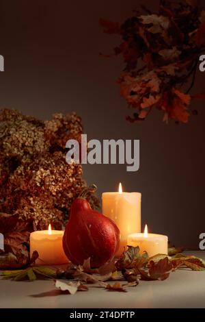 Stillleben mit Kürbis, ausgetrockneten Blättern und brennenden Kerzen. Im Hintergrund getrocknete Hortensienblüten und Eichenzweige. Herbstkonzept. Stockfoto
