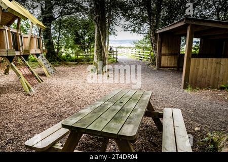 Picknickbank in einem bewaldeten Bereich mit vielen Bäumen und Sträuchern und anderen Holzkonstruktionen im Monty's Farm Park, Stockfoto