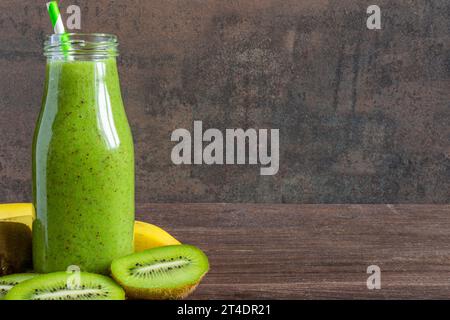 Grüner Smoothie aus Kiwis und Bananen in einer Glasflasche mit frischen Früchten auf rustikalem Holzhintergrund. Gesundes Diätgetränk Stockfoto