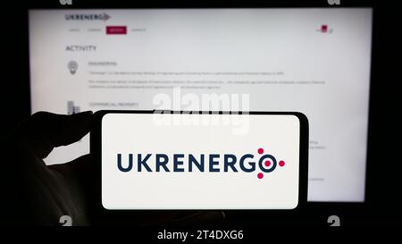 Person, die ein Handy mit dem Logo des ukrainischen Stromunternehmens Ukrenergo vor der Webseite hält. Schwerpunkt auf dem Display des Telefons. Stockfoto