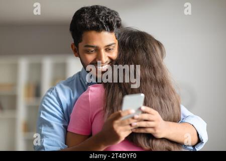 Ein indischer Mann umarmt seine Frau und benutzt heimlich das Telefon Stockfoto