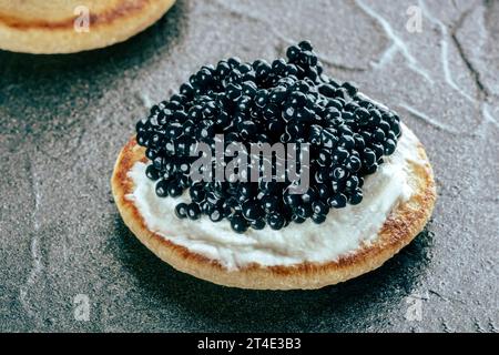 Eine Blini mit Kaviar und Frischkäse, eine Nahaufnahme auf schwarzem Schiefergrund Stockfoto