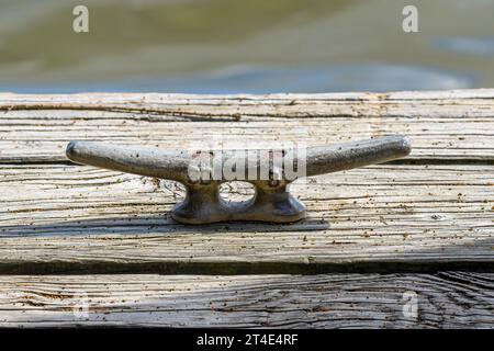 Nahaufnahme einer Metallklammer an einem hölzernen Dock mit verschwommenem Wasser im fernen Hintergrund Stockfoto