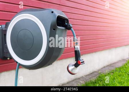 Einziehbare Schlauchtrommel Für Wandmontage. Moderner Gartenrasen Bewässerungsschlauch mit Sprinkler an der Hauswand. Rasen und Pflanzen Sie Bäume intelligente Bewässerung Stockfoto