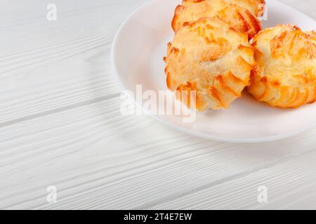 Goldene Profiteroles gefüllt mit Creme, serviert auf weißem Teller auf weißem Tisch aus nächster Nähe. Ein köstliches Dessert für jeden Anlass. Stockfoto