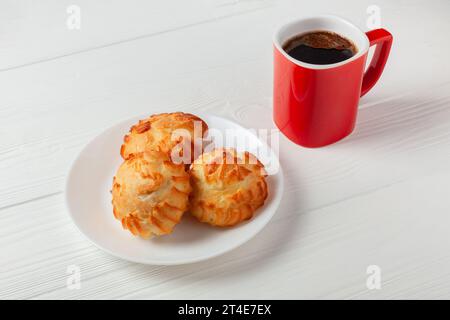 Goldene Profiteroles gefüllt mit Sahne, serviert mit einer Tasse Kaffee auf weißem Tisch. Ein köstliches Dessert für jeden Anlass. Stockfoto