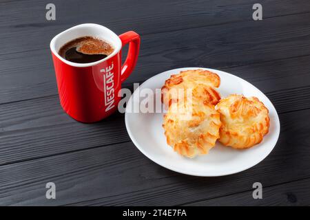 Goldene Profiteroles gefüllt mit Sahne, serviert mit einer Tasse Kaffee Nescafe auf dunklem Tisch. Ein köstliches Dessert für jeden Anlass. Ukraine, Khar Stockfoto