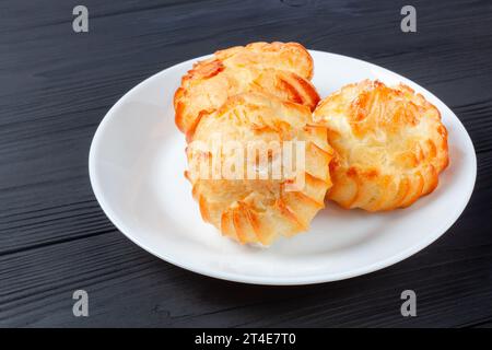 Goldene Profiteroles gefüllt mit Creme, serviert auf weißem Teller auf dunklem Tisch. Ein köstliches Dessert für jeden Anlass. Stockfoto