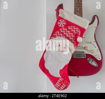 Weihnachtsdekoration, rote santa-Socke, die an einer roten E-Gitarre an einer weißen Wand hängt. Weihnachtskonzept. Kopierbereich. Horizontal Stockfoto
