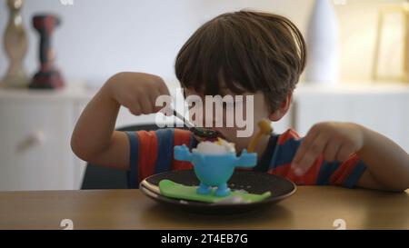 Ein kleiner Junge isst weich gekochtes Ei, oeuf a la coque. Das Kind isst eine leichte Mahlzeit allein mit einem Löffel Stockfoto