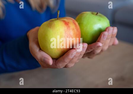 Die Frau hält Essen in der Hand. Das Mädchen hält einen Apfel. Äpfel in den Händen der Frau. Zwei grüne Äpfel Stockfoto