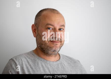 Ein Mann von gewöhnlichem Aussehen lächelt unrasiert und schaut auf grauen Hintergrund in die Kamera. Ein Mann in seinen 40ern. Stockfoto