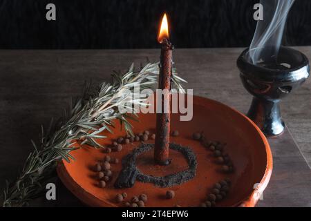 Traditionelles Ritual mit Feuer und schwarzer Kerze auf Tonplatte, begleitet von Pfeffer, Meersalz, Kräutern und Weihrauch Stockfoto