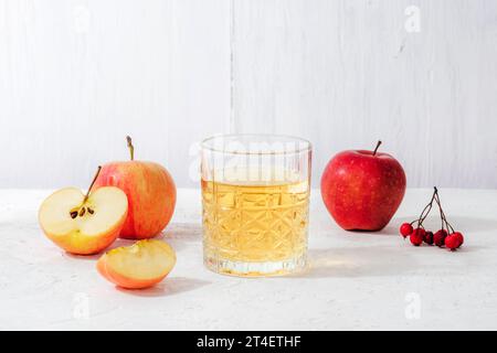 Frische reife Äpfel und ein Glas Apfelsaft oder Cidre auf weißem Tisch. Herbsternte, Thanksgiving-Konzept. Stockfoto