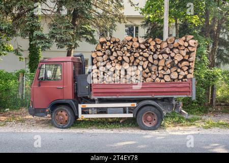 Kipper mit einer Leiche voller Brennholz. Lkw beladen mit Holzstämmen zur Lieferung für die Heizsaison. Brennholz für den Herd während der Stockfoto
