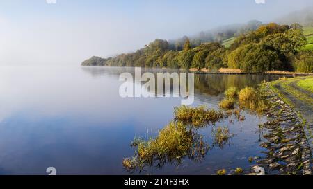 Ein Multi-Bild-Panorama von zwei Männern, die auf dem Balasee fischen, während sich der Nebel langsam um sie herum erhebt und atemberaubende Reflexionen im Wasser enthüllt. Stockfoto