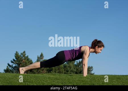 Fitte junge, sportliche Frau, die statische Plank-Übungen macht, Bauch- und Rückenmuskeln trainiert, im Stadtpark. Sportliche Frau beim Training, blauer Himmel zurück Stockfoto