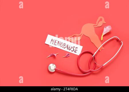 Wort-MENOPAUSE mit Papier Uterus, Blumenblättern und Stethoskop auf rotem Hintergrund Stockfoto