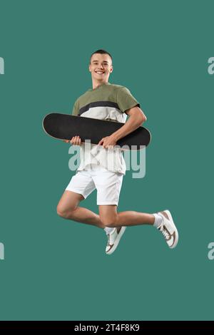 Hübscher junger Mann mit Skateboard-Sprung auf grünem Hintergrund Stockfoto