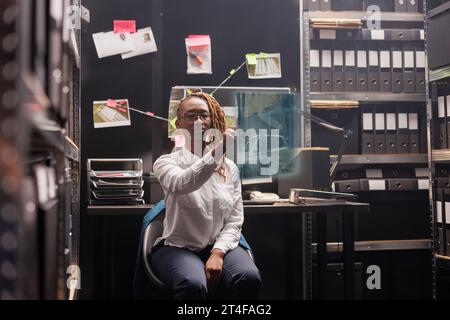 afroamerikanischer Detective untersucht holographisches Bild im Beweisraum, untersucht Hinweise und Erkenntnisse. Ermittlerin, die mit Augmented Reality und künstlicher Intelligenz arbeitet. Stockfoto