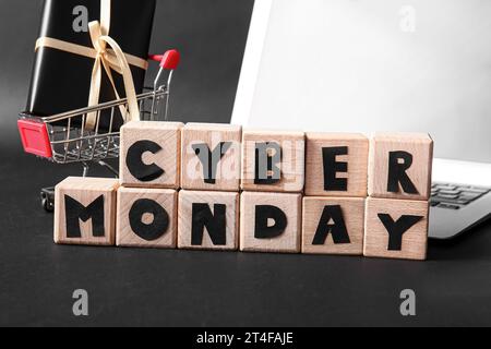 Text CYBER MONDAY aus Holzwürfeln, Warenkorb und Geschenkbox auf dunklem Hintergrund, Großansicht Stockfoto