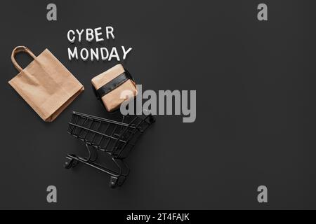 Komposition mit kleinem Einkaufswagen, Tasche und Geschenkbox auf dunklem Hintergrund. Cyber Monday-Angebot Stockfoto