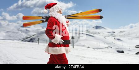 Der Weihnachtsmann geht und trägt Skier auf der Schulter auf einem verschneiten Hügel Stockfoto