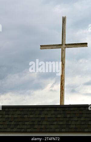 Ein rostendes Eisenkreuz auf einem Kirchengebäude hebt sich von einem stimmungsvollen, bewölkten Nachmittagshimmel ab. Stockfoto