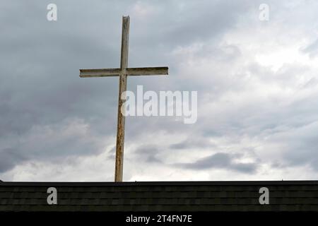 Ein rostendes Eisenkreuz auf einem Kirchengebäude hebt sich von einem stimmungsvollen, bewölkten Nachmittagshimmel ab. Stockfoto