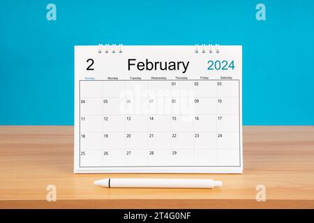 Monatlicher Schreibtischkalender im Februar für 2024 Jahre und Stift auf Holztisch mit blauem Hintergrund. Stockfoto