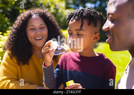 Glücklicher afroamerikanischer Vater, Mutter und Sohn blasen Blasen im sonnigen Garten, Kopierraum Stockfoto