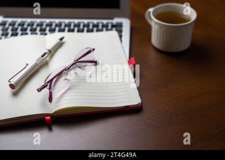 Brille auf Notizblock und Computer-Laptop und neben einer Tasse Tee. Kopierbereich. Stockfoto