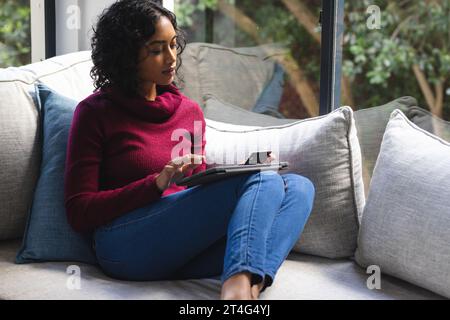 Glücklicher birassischer Mann, der im sonnigen Wohnzimmer mit Kreditkarte und Tablet auf dem Sofa sitzt Stockfoto