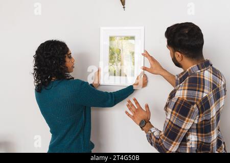 Fokussiertes birassisches Paar hängendes Bild an der Wand im Wohnzimmer zu Hause Stockfoto