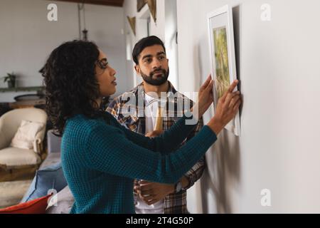 Fokussiertes birassisches Paar hängendes Bild an der Wand im Wohnzimmer zu Hause Stockfoto