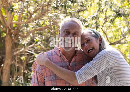 Porträt eines glücklichen älteren kaukasischen Paares, das sich im sonnigen Garten umschließt Stockfoto