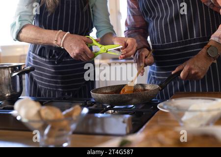 Mittelteil eines älteren kaukasischen Paares, das zu Hause in der Küche Abendessen kocht Stockfoto