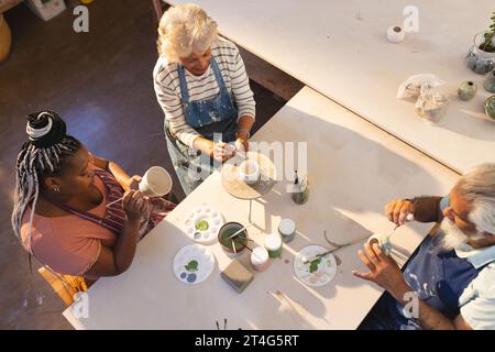Fröhliche Gruppe von Töpfern, die Tonkannen im Töpferstudio glasieren Stockfoto