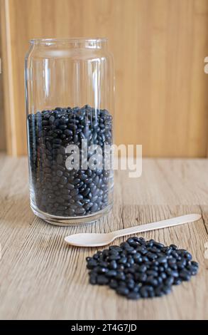 Schwarze Bohnen in einem klaren Glas, rohe Bohnen in einer Glasschale und ein Löffel auf dem Tisch. Schwarze Bohnen sind gut für die Gesundheit. Es ist eine Quelle von Protein, Ballaststoffen, A Stockfoto