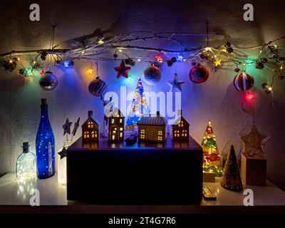 Neujahrsdekoration mit beleuchteten Spielzeughäusern und weihnachtsbäumen. Zweig mit hängenden Glaskugeln und Sternen, dekoriert mit glühenden Weihnachtslichtern. Stockfoto