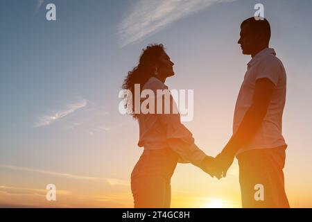 Das liebende Paar sieht sich vor dem Himmel bei Sonnenuntergang an Stockfoto