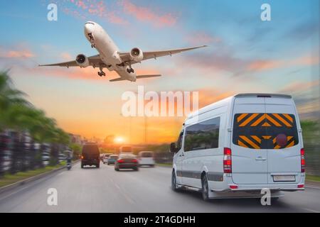 Der Minibus fährt neben anderen Autos am Abend am Sonnenuntergang entlang der Autobahn, ein Passagierflugzeug fliegt in den Himmel. Stockfoto