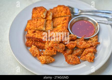 Thailändische Küche, frittierte Würstchen und frittiertes Schweinebrot mit süßer und scharfer Sauce. Nahaufnahme des traditionellen Frühstücks von Surat Thani Prov Stockfoto