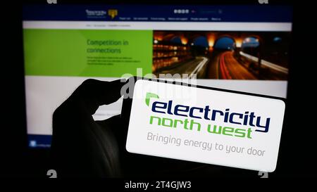 Person, die ein Mobiltelefon mit dem Logo des britischen Energieversorgers Electricity North West Limited vor der Website des Unternehmens hält. Schwerpunkt auf dem Display des Telefons. Stockfoto