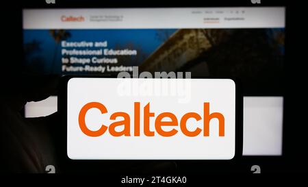 Person mit Handy und Logo des California Institute of Technology (Caltech) vor der Webseite. Schwerpunkt auf dem Display des Telefons. Stockfoto
